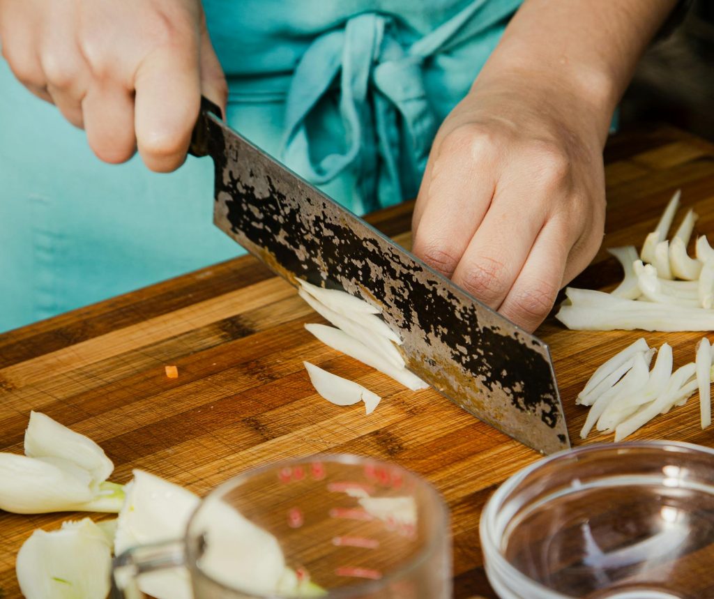 Close-up of chef's hands chopping onions on a wooden cutting board in a kitchen setting.