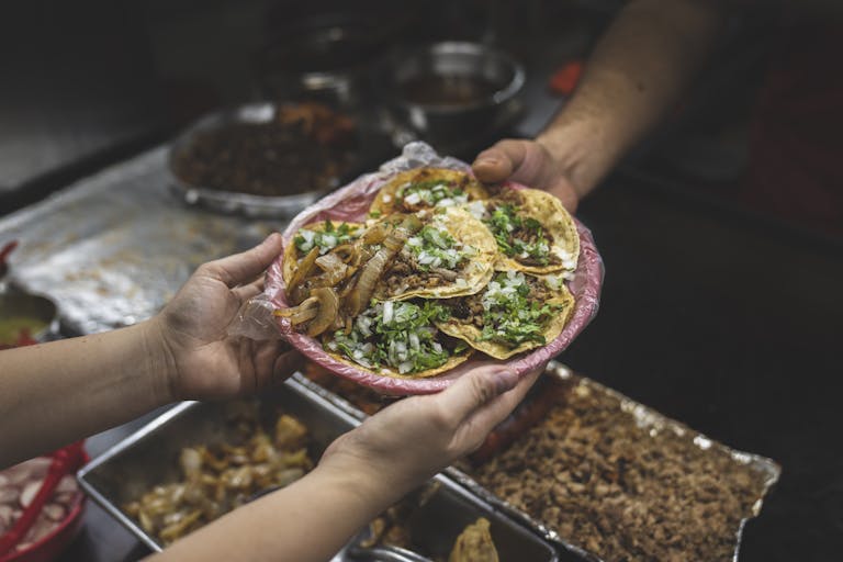 Freshly served authentic Mexican street tacos with onions and cilantro, handed over by vendor.